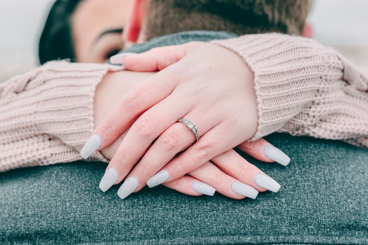 Close-up of woman's hands with an engagement ring embracing her partner in a cozy setting.